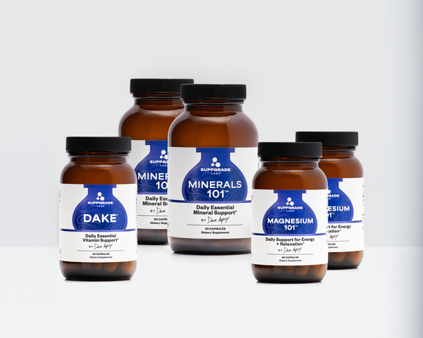 Five amber supplement bottles with black caps and white labels from Suppgrade Labs, arranged on a light gray background. The labels include Dake, Minerals 101, and Magnesium 101.