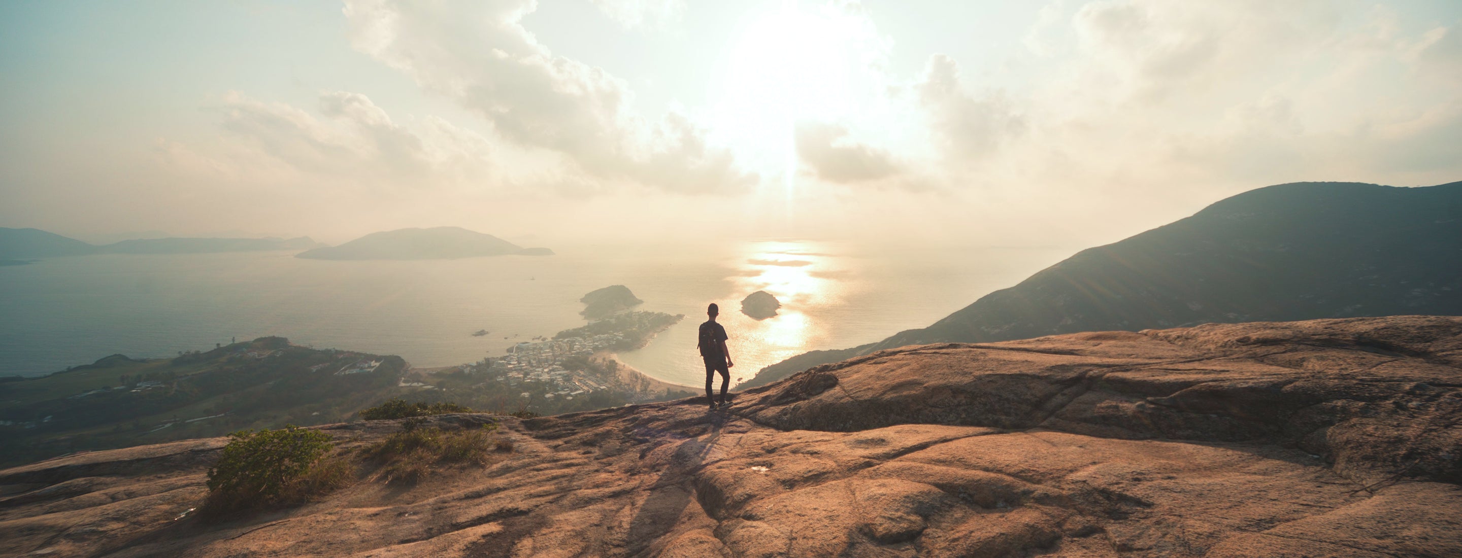 Image of a distant person overlooking a coastline from a mountain side.